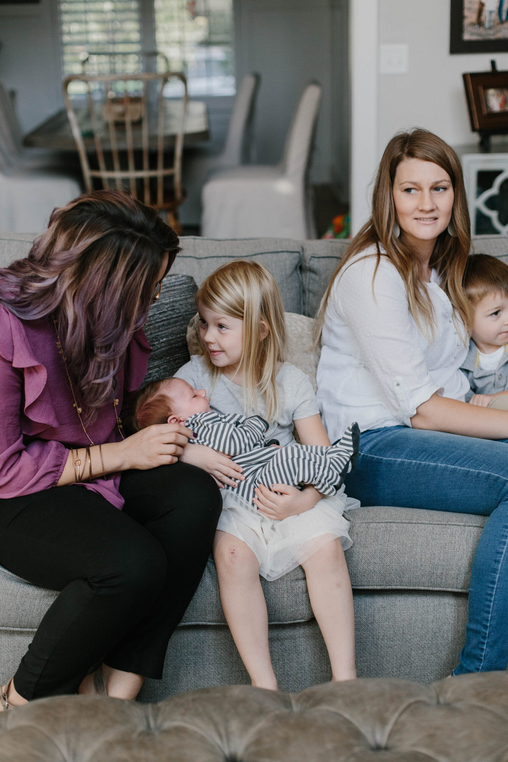 Young child holding a sleeping newborn on a couch beside two adults and another toddler